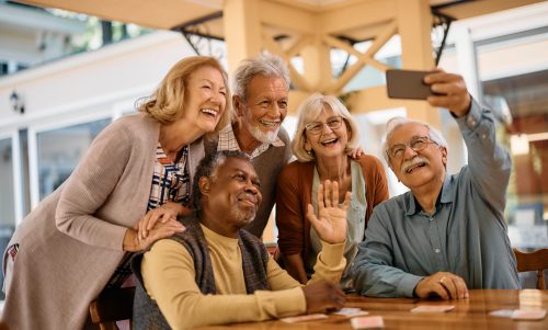 Cheerful group of seniors taking selfie with cell phone in residential care home.